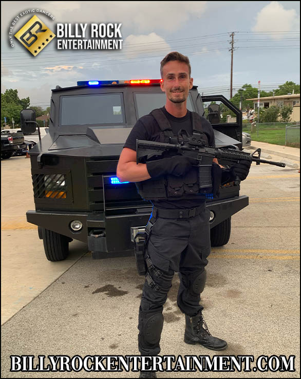 Alexander: Male dancer Alexander in tactical gear and rifle, standing in front of a black vehicle with emergency lights.